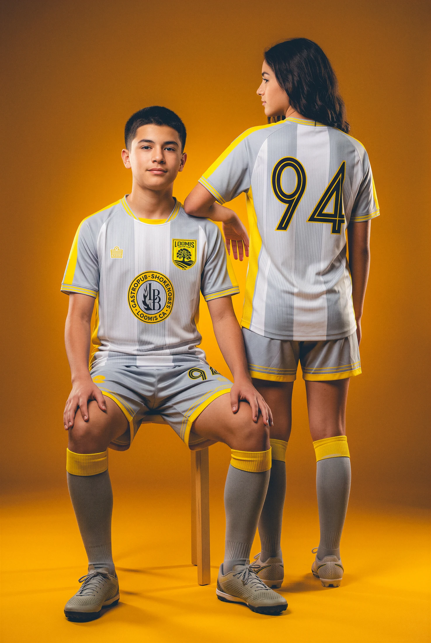 Two Loomis players presenting the away shirt against a gold backdrop