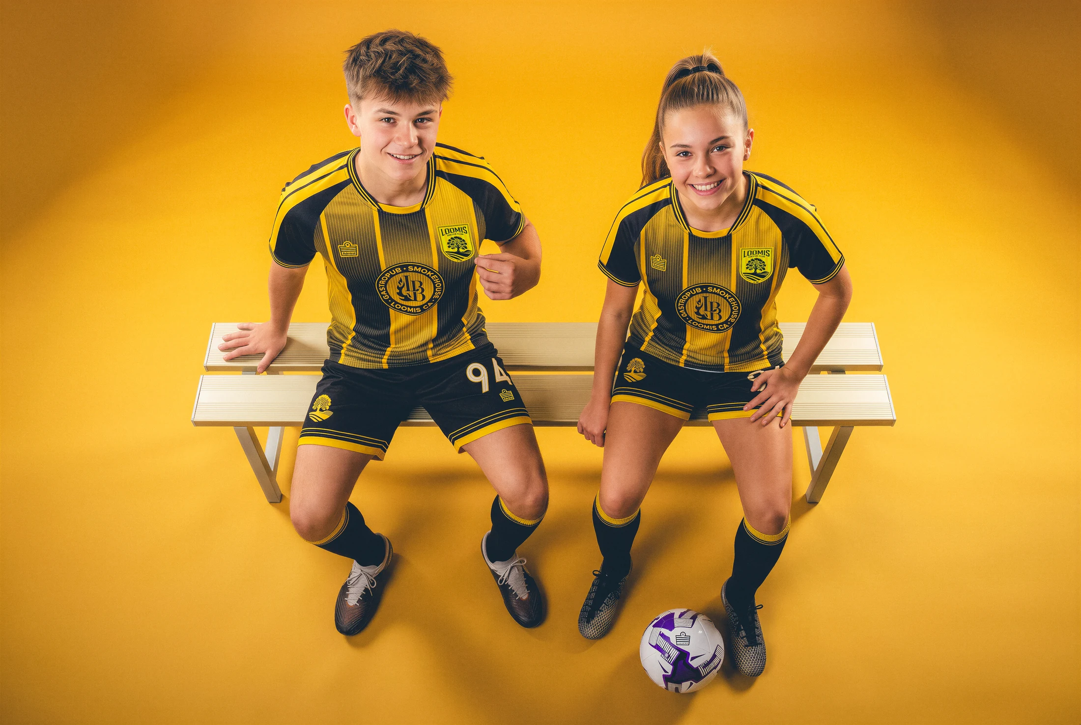 Two Loomis players in black-and-gold home shirts seated against a gold backdrop