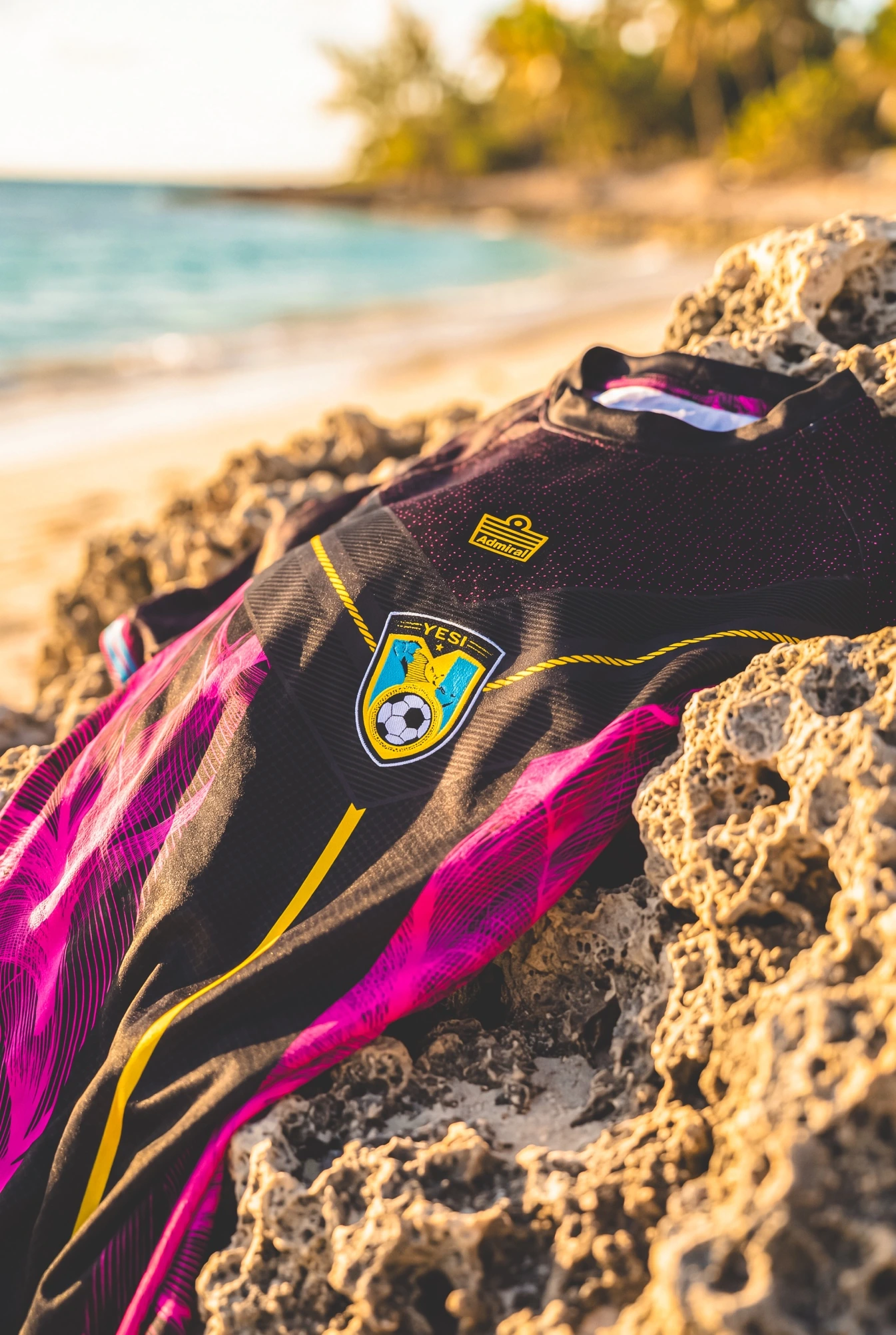 YESi Aqua and Flamingo anniversary jerseys arranged on coastal rock